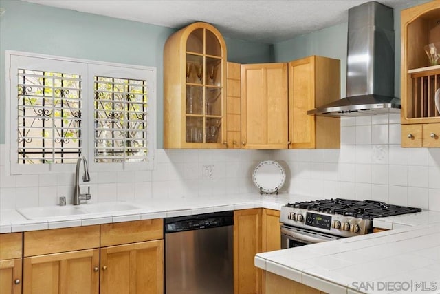 kitchen featuring stainless steel appliances, wall chimney range hood, sink, and tile countertops