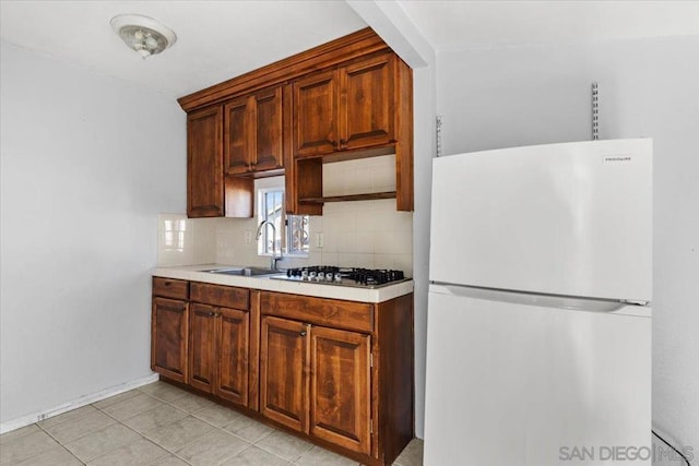 kitchen featuring white fridge, stainless steel gas cooktop, light tile patterned floors, sink, and backsplash