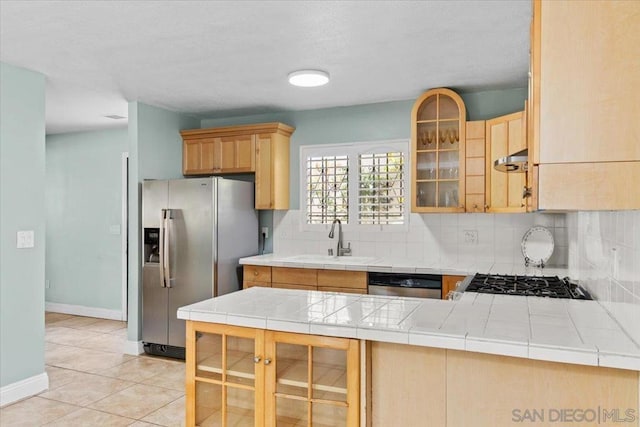 kitchen with sink, tile countertops, light tile patterned flooring, decorative backsplash, and appliances with stainless steel finishes