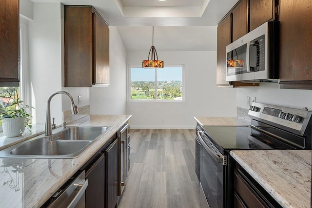 kitchen with stainless steel appliances, hanging light fixtures, light wood-style floors, a sink, and baseboards