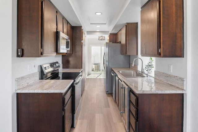 kitchen with appliances with stainless steel finishes, a sink, light wood-style flooring, and dark brown cabinetry