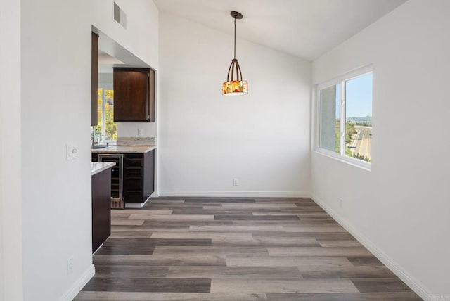 unfurnished dining area featuring lofted ceiling, baseboards, visible vents, and wood finished floors