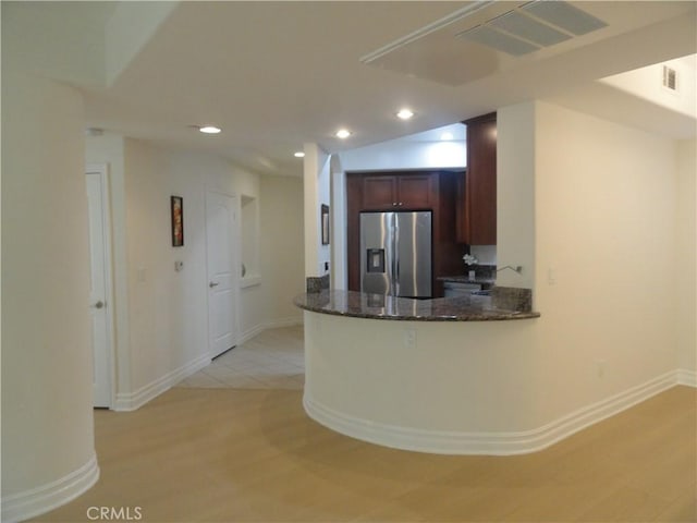 kitchen featuring kitchen peninsula, stainless steel refrigerator with ice dispenser, dark stone counters, and light tile patterned floors