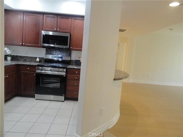 kitchen featuring decorative backsplash, light tile patterned floors, appliances with stainless steel finishes, and dark stone countertops