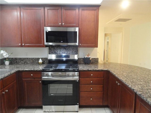 kitchen featuring stainless steel appliances, dark stone counters, kitchen peninsula, and light tile patterned flooring