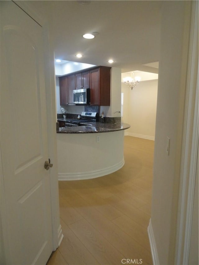 kitchen with stainless steel appliances, dark stone countertops, backsplash, kitchen peninsula, and a chandelier