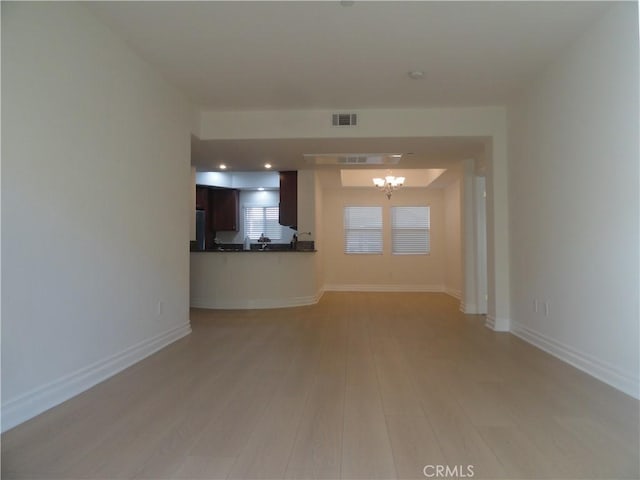 unfurnished living room featuring light wood-type flooring and an inviting chandelier