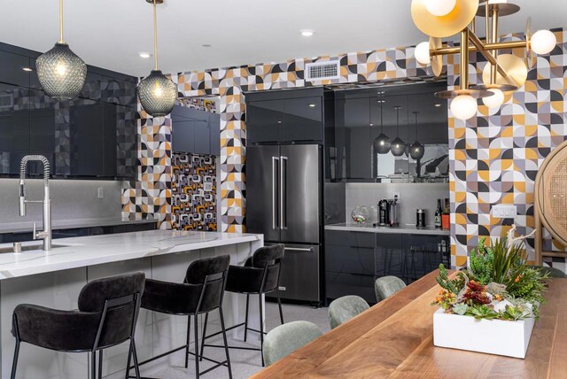 kitchen featuring sink, a breakfast bar area, hanging light fixtures, light stone countertops, and high end refrigerator