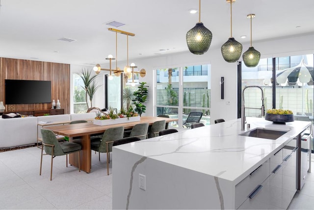 kitchen featuring sink, decorative light fixtures, white cabinetry, light stone countertops, and a kitchen island with sink