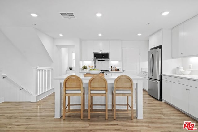 kitchen with stainless steel appliances, white cabinetry, light wood-type flooring, and a breakfast bar