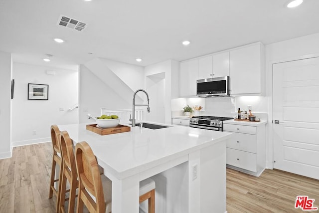 kitchen with a center island with sink, a kitchen bar, white cabinets, appliances with stainless steel finishes, and sink