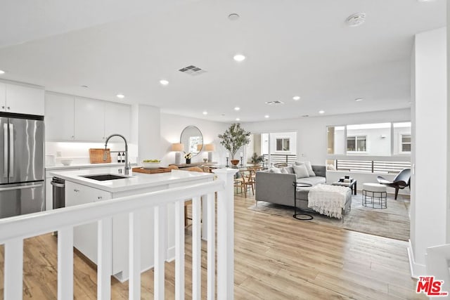 kitchen featuring stainless steel refrigerator, white cabinets, light hardwood / wood-style floors, and sink