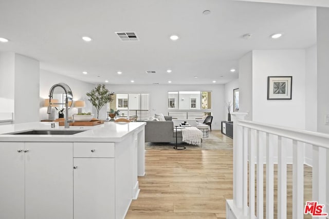 kitchen featuring sink, white cabinets, light hardwood / wood-style floors, and an island with sink