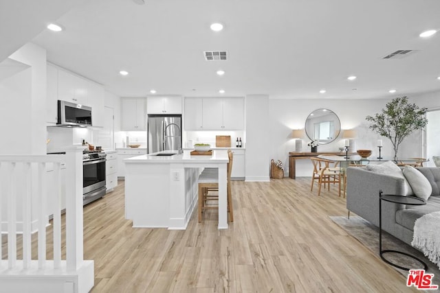 kitchen with a center island with sink, white cabinetry, light wood-type flooring, and appliances with stainless steel finishes