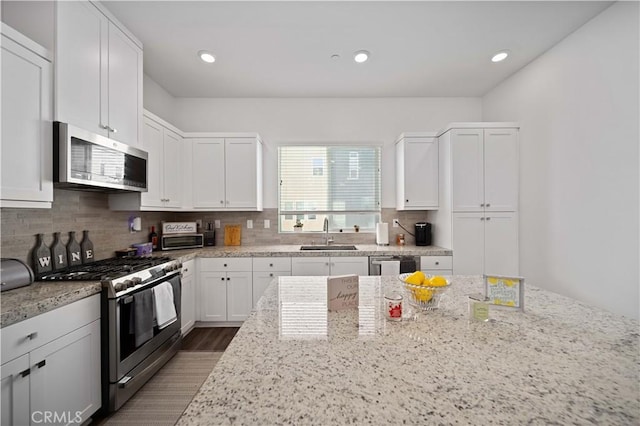 kitchen with light stone countertops, appliances with stainless steel finishes, white cabinetry, and sink