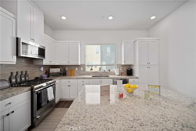 27014 Hummingbird Ln, Valencia, CA 91381 - kitchen with white cabinetry, stainless steel appliances, backsplash, a sink, and light stone counters