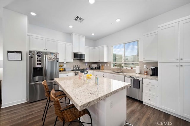 kitchen featuring a center island, white cabinets, appliances with stainless steel finishes, a kitchen breakfast bar, and sink