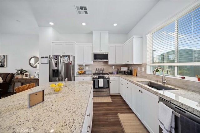 kitchen featuring stainless steel appliances, light stone countertops, decorative backsplash, sink, and white cabinetry