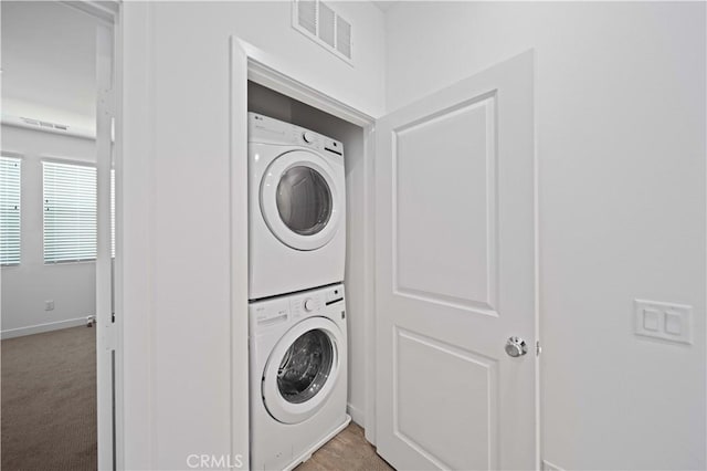 clothes washing area with light colored carpet and stacked washing maching and dryer