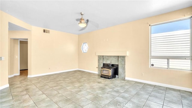 unfurnished living room featuring light tile patterned flooring, ceiling fan, and a wood stove