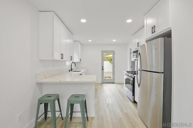 kitchen featuring kitchen peninsula, light stone countertops, white cabinets, appliances with stainless steel finishes, and sink