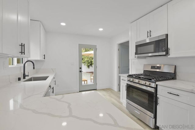 kitchen with light stone counters, light hardwood / wood-style flooring, white cabinets, appliances with stainless steel finishes, and sink