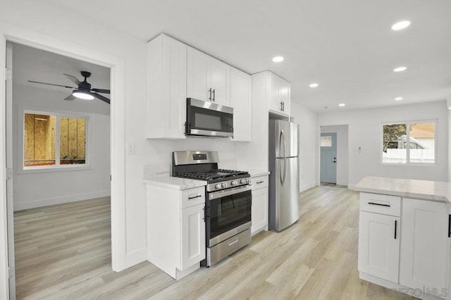 kitchen featuring white cabinetry, light stone counters, ceiling fan, light hardwood / wood-style flooring, and appliances with stainless steel finishes