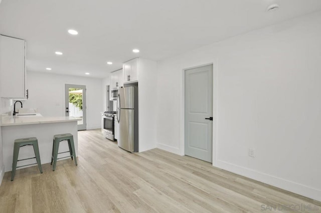 kitchen featuring a kitchen breakfast bar, stainless steel appliances, kitchen peninsula, white cabinets, and sink