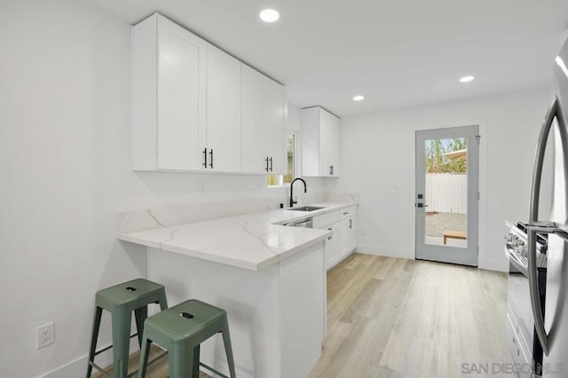 kitchen with light stone countertops, white cabinetry, a kitchen bar, and sink