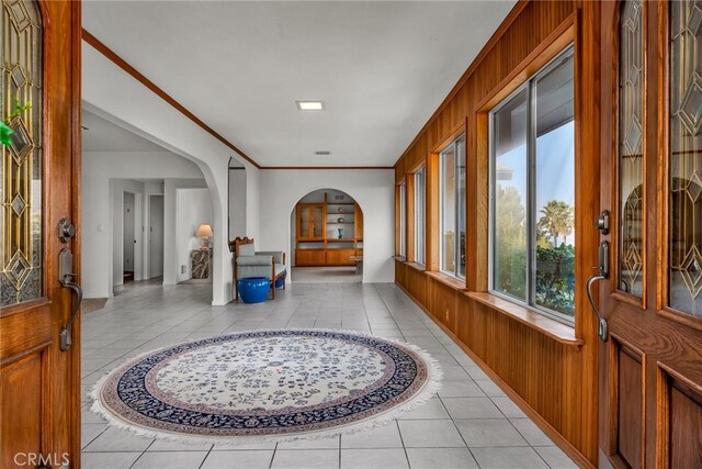 entrance foyer with ornamental molding, wooden walls, and light tile patterned flooring