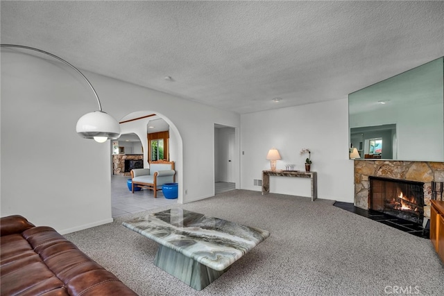 carpeted living room featuring a stone fireplace and a textured ceiling