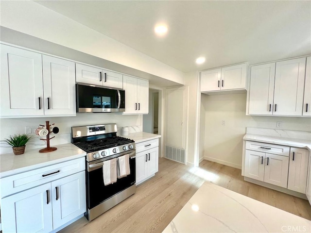 kitchen featuring visible vents, light wood-type flooring, light stone counters, white cabinetry, and appliances with stainless steel finishes