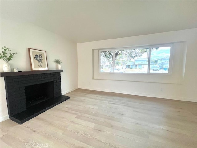 unfurnished living room with lofted ceiling, light wood-style flooring, a fireplace, and baseboards