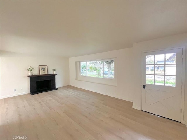 unfurnished living room featuring a brick fireplace, light wood-type flooring, and baseboards