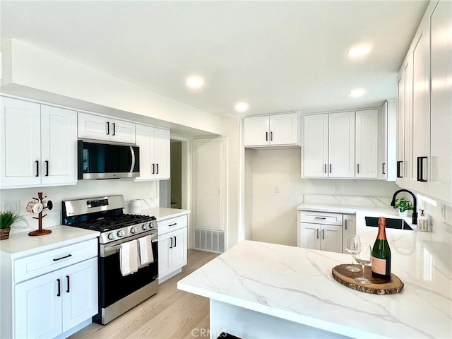 kitchen with visible vents, light stone countertops, white cabinets, stainless steel appliances, and a sink