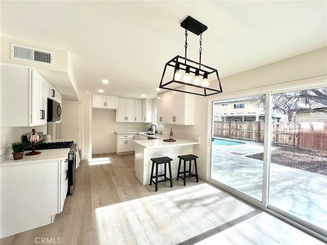 kitchen with stainless steel gas range oven, visible vents, a sink, a peninsula, and white cabinets