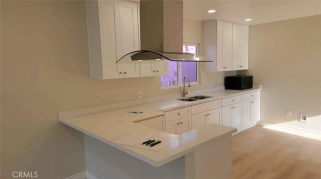 kitchen featuring kitchen peninsula, island exhaust hood, light wood-type flooring, white cabinetry, and sink