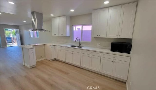 kitchen with island exhaust hood, light wood-type flooring, kitchen peninsula, sink, and white cabinetry