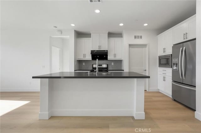 kitchen featuring light hardwood / wood-style floors, a kitchen island with sink, backsplash, white cabinets, and appliances with stainless steel finishes