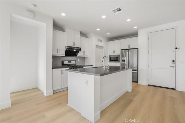 kitchen with appliances with stainless steel finishes, an island with sink, white cabinets, light hardwood / wood-style flooring, and sink