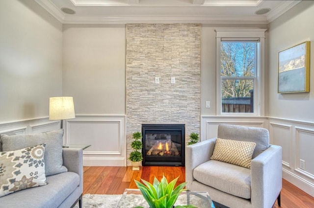 living room featuring hardwood / wood-style flooring, ornamental molding, and a stone fireplace