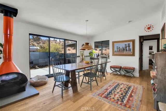 dining room featuring lofted ceiling, light wood-style floors, and a wood stove