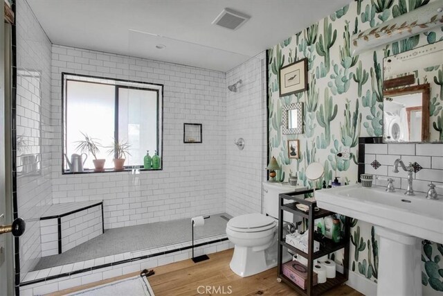 bathroom with visible vents, toilet, wood finished floors, tile walls, and tiled shower