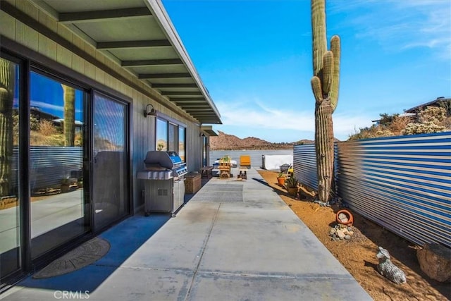 view of patio with area for grilling, fence, and a water view