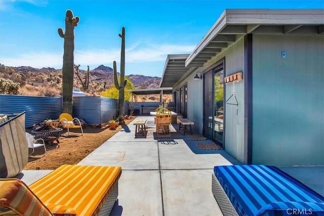 view of patio / terrace featuring fence, a mountain view, and an outdoor fire pit