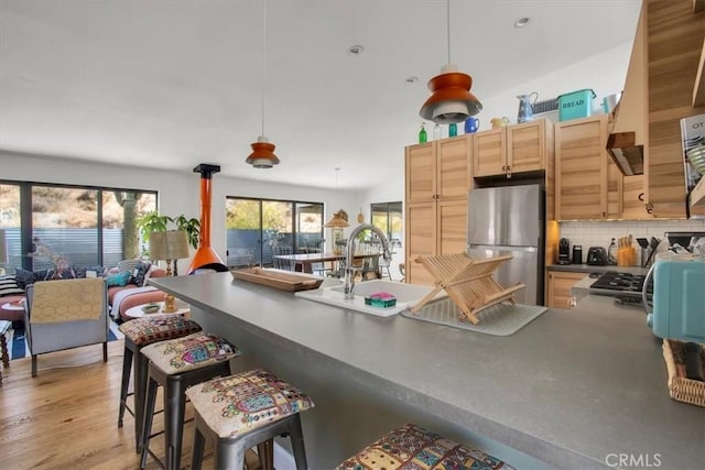 kitchen featuring dark countertops, backsplash, light wood-type flooring, freestanding refrigerator, and a sink