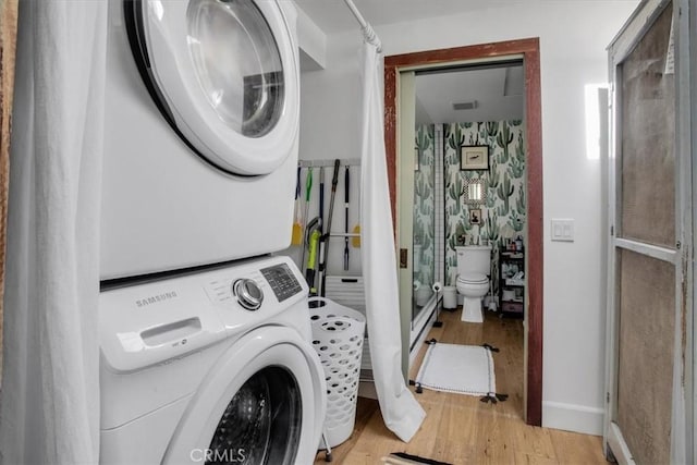 laundry area featuring light wood finished floors, stacked washer / dryer, laundry area, and baseboards