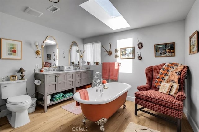 bathroom with visible vents, toilet, a skylight, wood finished floors, and a sink