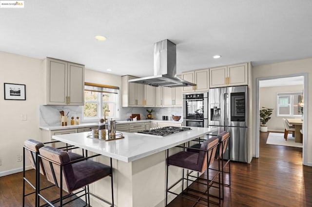 kitchen with island range hood, a breakfast bar area, stainless steel appliances, dark hardwood / wood-style floors, and tasteful backsplash