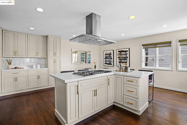 kitchen with dark wood-type flooring, island range hood, a kitchen island, stainless steel gas cooktop, and a breakfast bar area